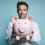 Uśmiechnięty mężczyzna trzymający świnkę skarbonkę przed sobą