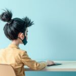 Osoba siedząca tyłem w maseczce i zamkniętymi rozmazanymi oczami. Najprawdopodobniej coś ukrywająca, albo kłamiąca. Oszust